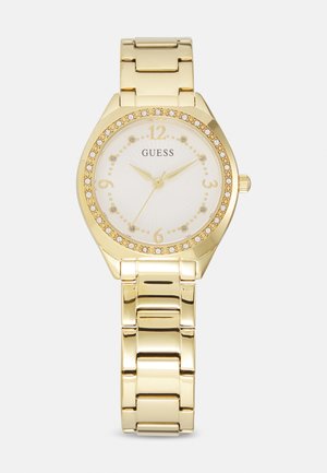 Orologio da polso in tono oro con cinturino in metallo lucido, cassa ottagonale, quadrante bianco, indici delle ore dorati e accenti scintillanti attorno alla lunetta.