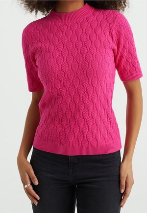 Fuchsia gebreide trui met een textuur van bladeren, een geribde halslijn en zoom, en korte mouwen. Gecombineerd met zwarte jeans.