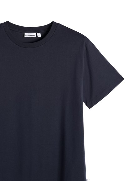 Σκούρο ναυτικό μπλε κοντομάνικο T-shirt με στρογγυλή λαιμόκοψη, απλωμένο επίπεδα, που δείχνει το πάνω μέρος του κορμού και το μανίκι με την ετικέτα της μάρκας J.LINDEBERG στο εσωτερικό του γιακά.