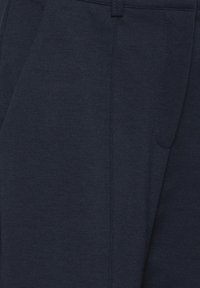 Dark navy blue tailored trousers with side pockets and belt loops, showing fabric texture and stitching details.