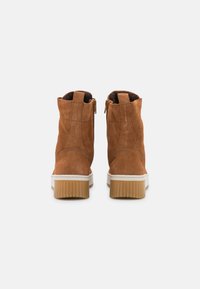 Bottines en suede marron avec une semelle intermédiaire blanche, présentant une fermeture éclair et une semelle en caoutchouc texturée. Design simple avec des détails cousus.