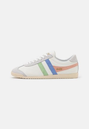 Baskets basses blanches à rayures vertes, bleues et pêche, semelle beige, accents gris à l’avant et au talon, avec le logo « Gola » sur le côté.