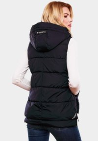 Gilet matelassé noir avec capuche, présentant un design matelassé, des poches latérales et une étiquette de logo à l'arrière. Porté par-dessus un haut à manches longues léger.