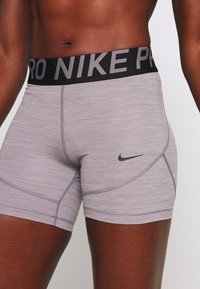Grå atletiska shorts med ett svart elastiskt midjeband som har "PRO NIKE" i grå text. Tillverkade av slätt, figurnära tyg med subtil struktur.