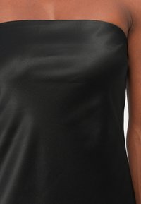 Blusa negra sin mangas con una textura suave y elegante y una silueta ajustada. La tela tiene un acabado brillante. Diseño sencillo sin adornos.
