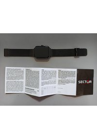 Orologio smartwatch nero con quadrante rettangolare e bracciale in maglia, accanto a un manuale utente piegato che presenta istruzioni multilingue e dettagli sulla garanzia.