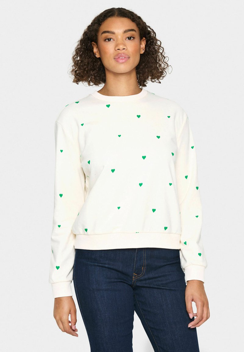 Sudadera crema con cuello redondo, manga larga y patrones de corazones verdes distribuidos uniformemente por toda la tela. Dobladillo y puños acanalados.