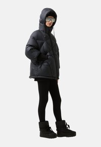 Sort pufferjakke med quilted design, overdimensioneret hætte og frontlynlås. Kombineret med sorte leggings og isolerede ankelstøvler.