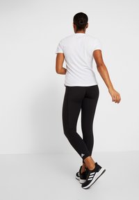 Leggings negros y una camiseta blanca, con un diseño ajustado. Los leggings tienen un pequeño logo en el tobillo, y la camiseta tiene un corte clásico.