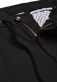 Schwarze Sportshorts mit einem Kordelzug am Bund, Knopfverschluss und einem Reißverschluss. Innenfutter aus einem gemusterten Stoff in Blau und Orange.