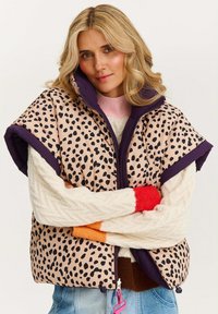 Padded vest w jasnoróżowym kolorze z czarnym leopardzim nadrukiem, fioletowym kołnierzem i zapięciem na zamek. Warstwowany z kremowym swetrem dzianinowym i kolorowymi rękawami.