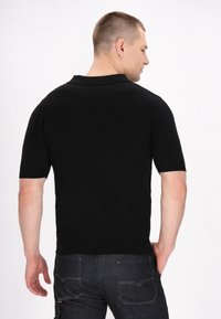 Černé polo tričko s krátkým rukávem a pletenou strukturou, s klasickým límcem a přiléhavým střihem, spárované s tmavými džínami.