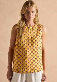 Kollane puuvillane ilma varrukateta topp, millel on punane ja sinine lillemuster. Omab ümarat kaelust ja vabalt langevat lõiget.