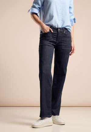 Des jeans en denim foncé à coupe droite présentent un design classique à cinq poches, des coutures contrastantes et une texture subtile. Portés avec des baskets blanches.