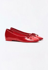 Ballerines rouges brillantes à bouts ronds, avec petits nœuds sur le dessus et talons plats bas, placées côte à côte sur un fond blanc uni.