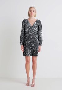 Vestido curto de lantejoulas em cinza-prateado, com decote em V, mangas longas e silhueta justa. Realçado com detalhes refletivos cintilantes.