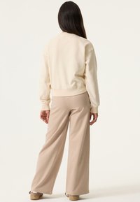 Sudadera beige corta con puños y dobladillo acanalados, combinada con pantalones de pierna ancha y rayas en tonos marrón claro, que muestran una textura suave y un ajuste relajado.