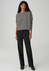 Maglione a righe bianche e nere, vestibilità ampia, scollo rotondo, abbinato a pantaloni neri a vita alta e scarpe nere basse.