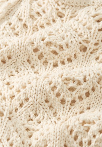 Tissu tricoté couleur crème avec un motif en losanges et câbles comportant de petits trous ouverts dans un design texturé.