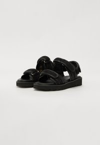 Sorte tekstil sandaler med tykke sorte gummisåler, med brede stropper og teksturert detaljering. Justerbare lukkinger for en sikker passform.
