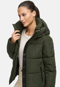 Veste en duvet verte avec capuche, fermeture éclair à l'avant et deux poches latérales. Présente une finition brillante et un patch logo sur la manche.