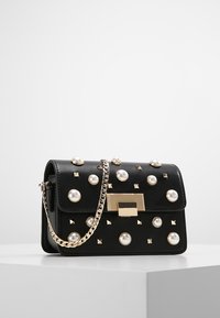 Borsa a tracolla in pelle nera decorata con borchie rotonde e a piramide, hardware dorato e una tracolla a catena. Forma rettangolare con chiusura a pattina.