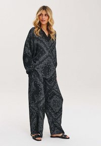 Czarny i biały zestaw w wzór paisley, składający się z luźnej koszuli i spodni o szerokich nogawkach, z gładkiego materiału i swobodnym kroju.