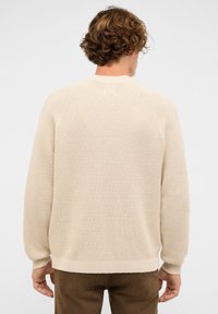 Beige Strickpullover mit strukturiertem Muster, geripptem Kragen, Bündchen und Saum. Besitzt Raglanärmel und eine lockere Passform.