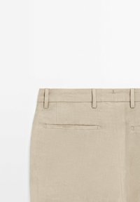 Beige Hose aus einem glatten, strukturierten Stoff. Verfügt über Gesäßtaschen mit verdeckten Öffnungen und Gürtelschlaufen. Schlichtes, tailliertes Design.