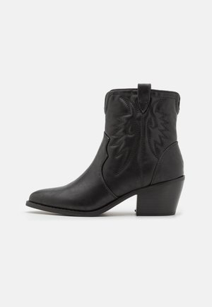 Botte de cowboy noire en cuir montant à la cheville avec un talon bas empilé et une couture décorative en zigzag sur le dessus.