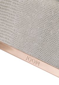 Tekstil med struktureret lysegrå overflade og et mønster, prydet med en rosaguld kant langs bunden, hvor "JOOP!" er præget.