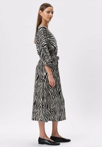 Sukienka w czarno-białe paseczki w zebra z rękawami 3/4, wcięciem w talii i długości midi, zestawiona z czarnymi balerinami.