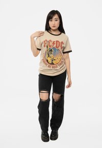 Beige AC/DC graphic t-shirt with brown ringer accents, featuring a vibrant print. Black ripped jeans and black platform boots complete the outfit.