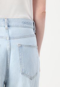 Lyseblå denimjeans med høy midje, utstyrt med et sydd merke "2NDDAY" på bakskjorten og to baklommmer.