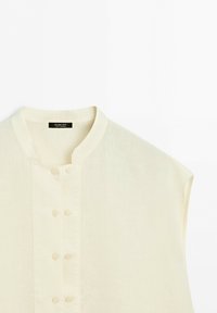 Off-white mouwloos shirt met een mandarijnkraag en vier paar bedekte knopen middenvoor.