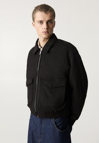 Giubbotto bomber nero in tessuto testurizzato, con chiusura a zip sul davanti, colletto a punta, due tasche frontali e vita elasticizzata, dal fit morbido.