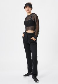 Czarny siateczkowy crop top z długim rękawem w połączeniu z czarnymi joggerami z elastycznym pasem i bocznymi kieszeniami. Uzupełniony czarnymi butami sportowymi.