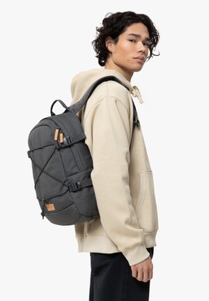 Mochila de color gris oscuro con tela texturizada, correas ajustables y detalles de cuero. Presenta un sistema de cordón elástico en la parte delantera y bolsillos laterales.