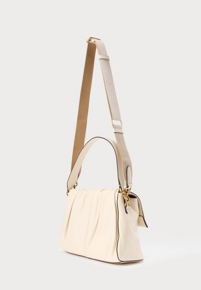 Skuldertaske i cremefarvet med et samlet design, sort piping og to stropper: den ene i tanfarvet stof, den anden i matchende cremefarvet materiale.