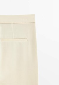 Pantaloni color crema con una texture liscia, dotati di una tasca posteriore, design slim-fit e linee pulite.