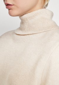 Maglione girocollo beige chiaro realizzato in morbido tessuto lavorato a maglia. Presenta un collo a costine e una vestibilità comoda. Texture liscia con dettagli minimi.