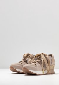 Scarpe da ginnastica beige con tomaia in suede testurizzato, lacci piatti e tacco a zeppa con dettagli intrecciati. Suola intermedia bianca e suola esterna in gomma.