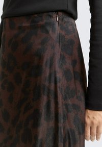 Jupe avec motif léopard brun et noir, au toucher lisse, dotée d'une fermeture éclair sur le côté, d'une coupe mi-longue et d'une taille cintrée.