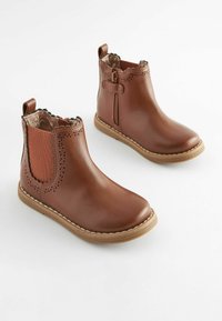 Botas de cuero marrón hasta el tobillo con bordes festoneados, cremallera lateral, panel elástico y suela texturizada; perforaciones decorativas cerca del tobillo.