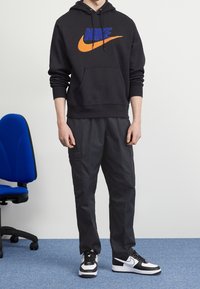 Svart hoodie med orange och blå Nike-logga, kombinerad med mörkgrå cargobyxor och svarta och vita Nike-skor; mjuk tyg, pullover-design.
