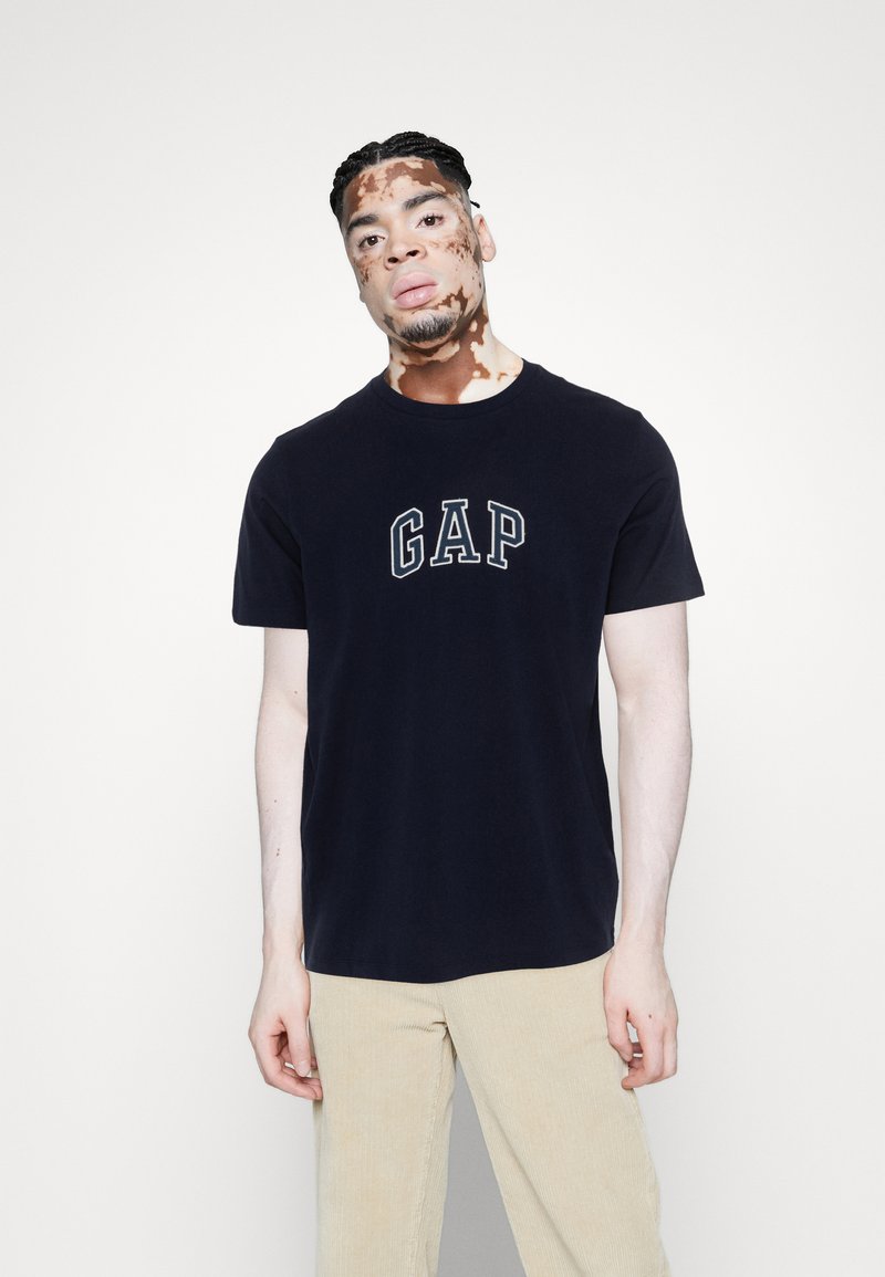 Marineblå bomulls T-skjorte med "GAP" logo i lys grå, rund hals, korte ermer, sammen med beige kordfløyelsbukser.
