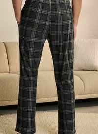 Black and gray plaid pants with an elastic waistband, featuring a textured fabric and straight legs, resting on a light-colored rug.