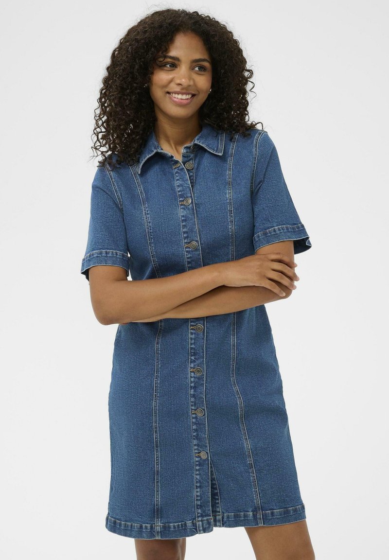 Robe en jean à manches courtes, avec un boutonnière à l'avant et une forme légèrement cintrée. Caractéristiques de coutures verticales et d'un bas ourlé.