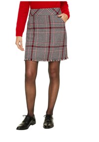 Wollmischung Karierten Rock mit rot, schwarz und weißen Mustern, fransigem Saum und zwei seitlichen Taschen. Kombiniert mit schwarzen Halbschuhen und Strumpfhosen.