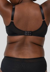 Zwart lingeriesetje met een doorschijnende bh met verstelbare bandjes en een haaksluiting, aangevuld met bijpassende high-waisted shorts.